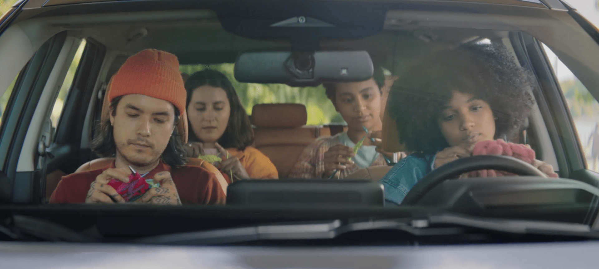 Four people sit in a parked car, each engaged in knitting