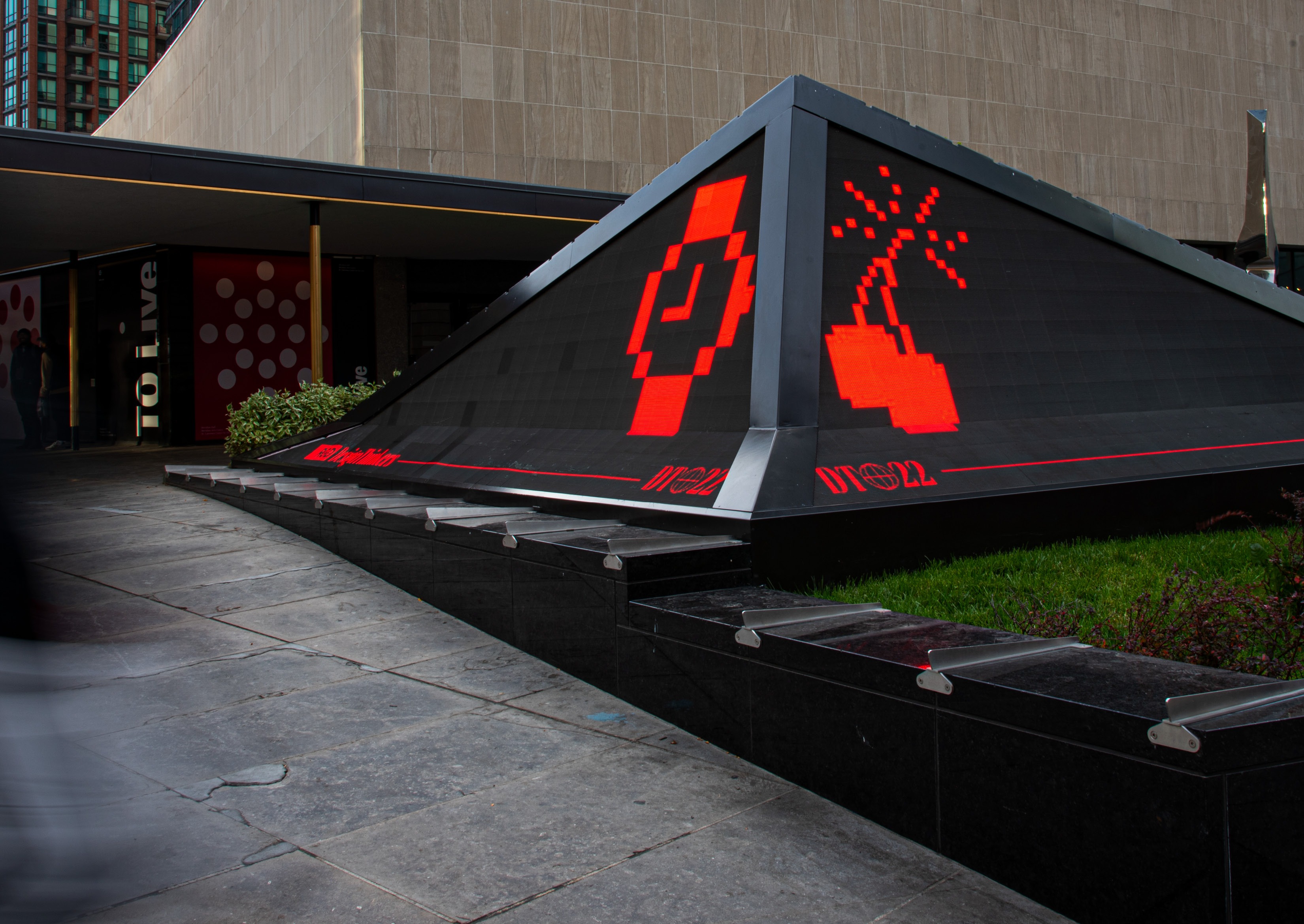 Red pixelated icons of a watch and an explosion displayed on an angled outdoor installation