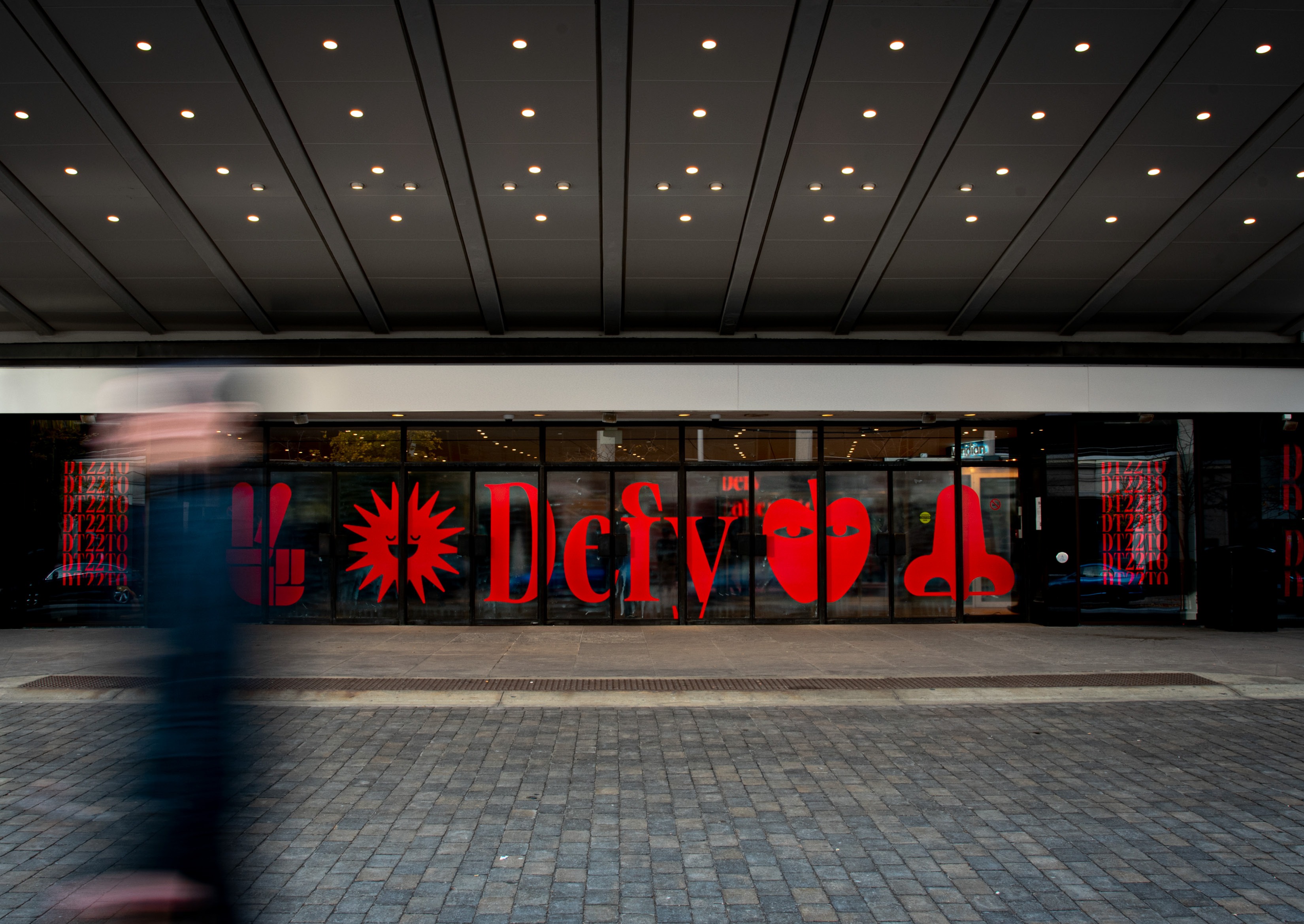 Entrance of the 2022 RGD DesignThinkers conference featuring large red 'Defy' lettering and bold icons on glass windows, promoting creativity and defiance