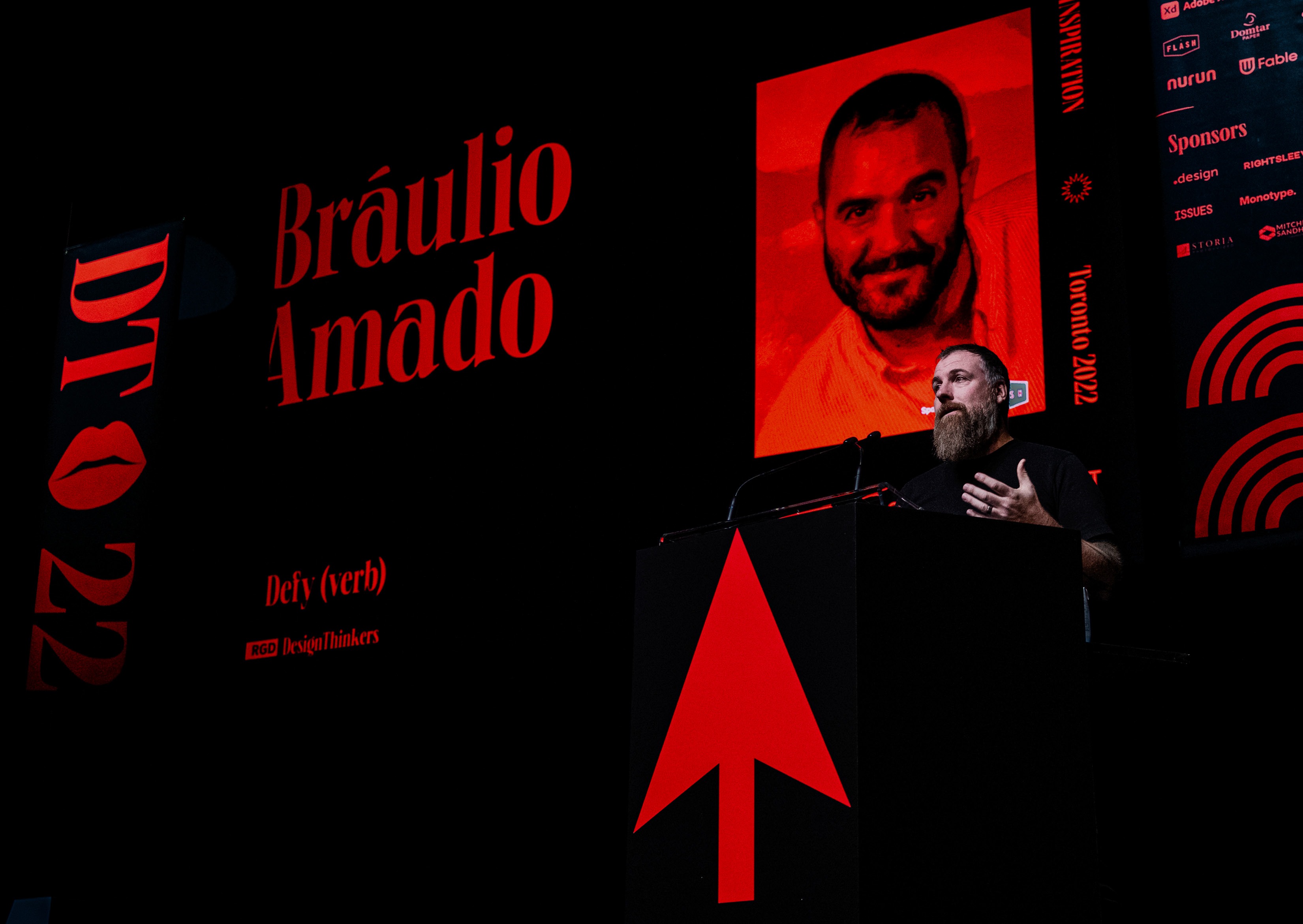 Speaker Bráulio Amado presenting on stage, with his name in bold red lettering on a black background