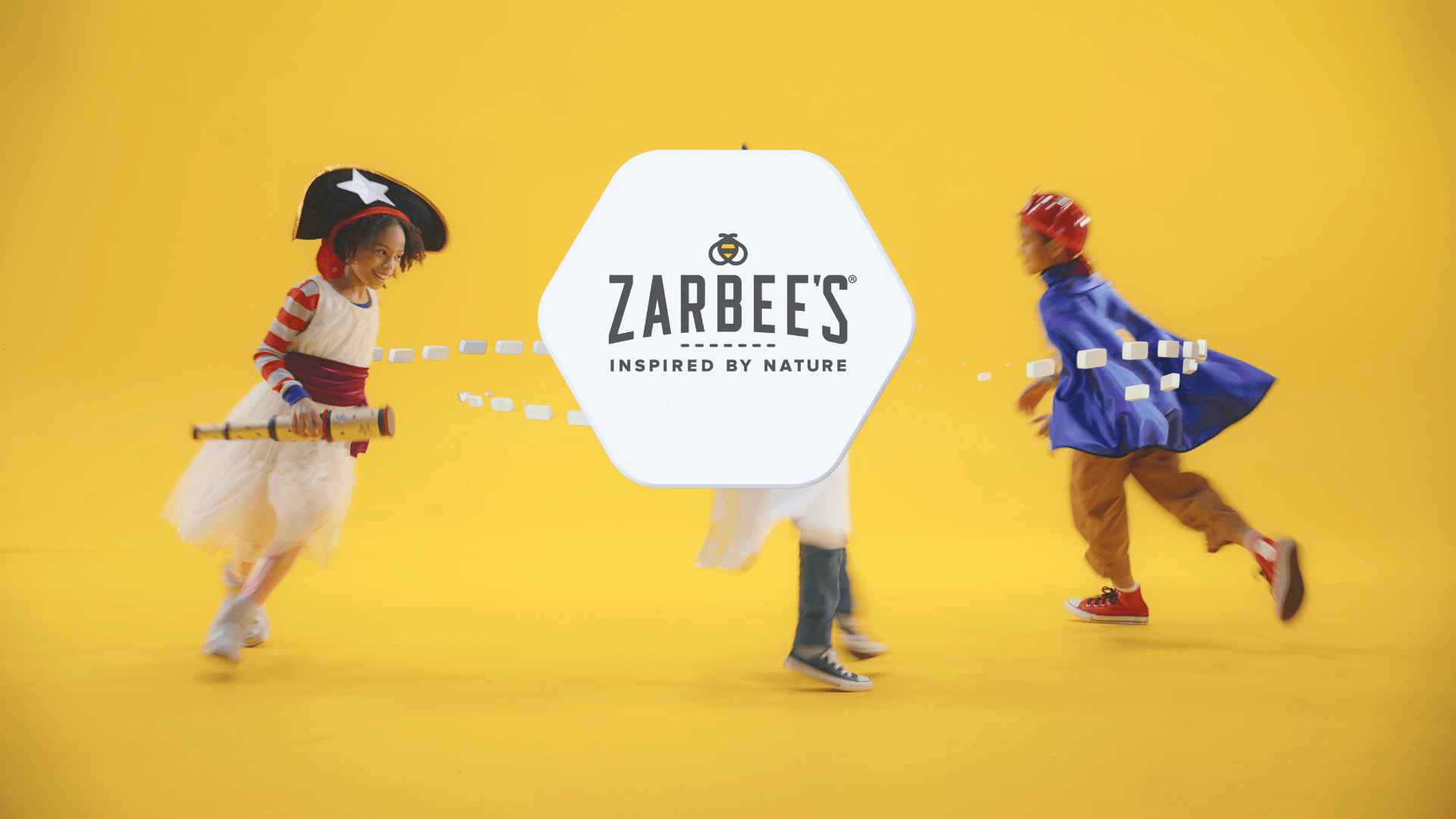 Two children in costumes run joyfully, playing with a telescope, with the Zarbee's logo in the center on a yellow background